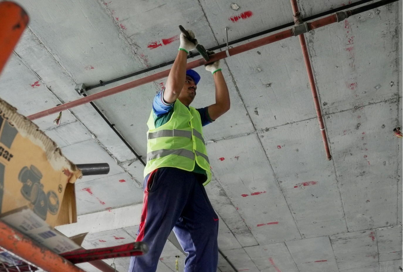 Construction worker in hard hat and safety vest working on overhead pipe system